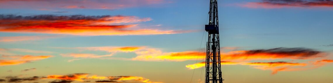 oil derrick in foreground with sun setting behind the rig