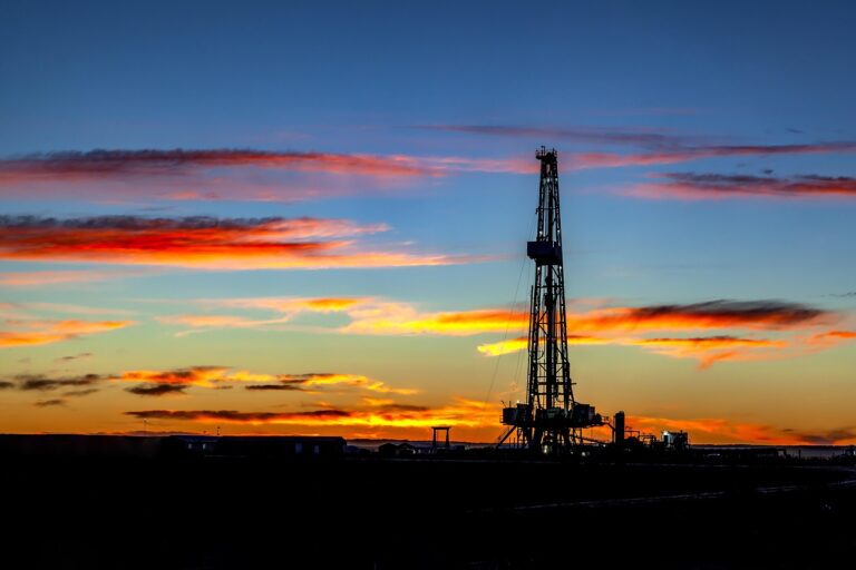 oil derrick in foreground with sun setting behind the rig