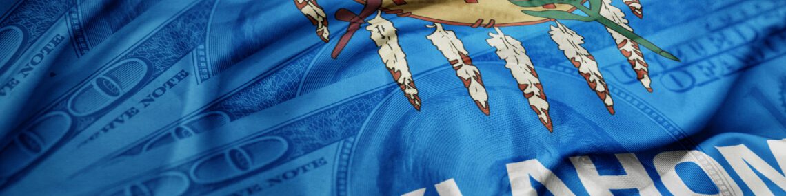 waving colorful oklahoma state flag on the dollar money background. finance concept. macro shot