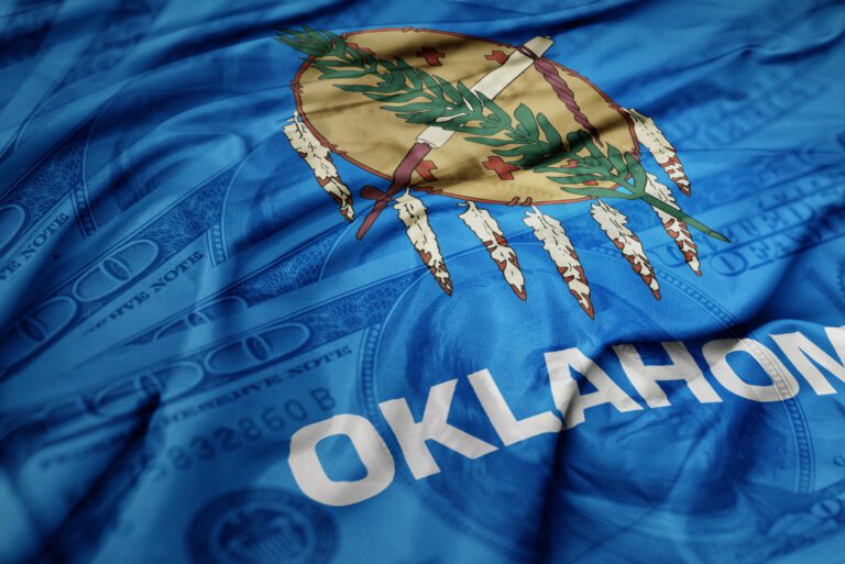 waving colorful oklahoma state flag on the dollar money background. finance concept. macro shot