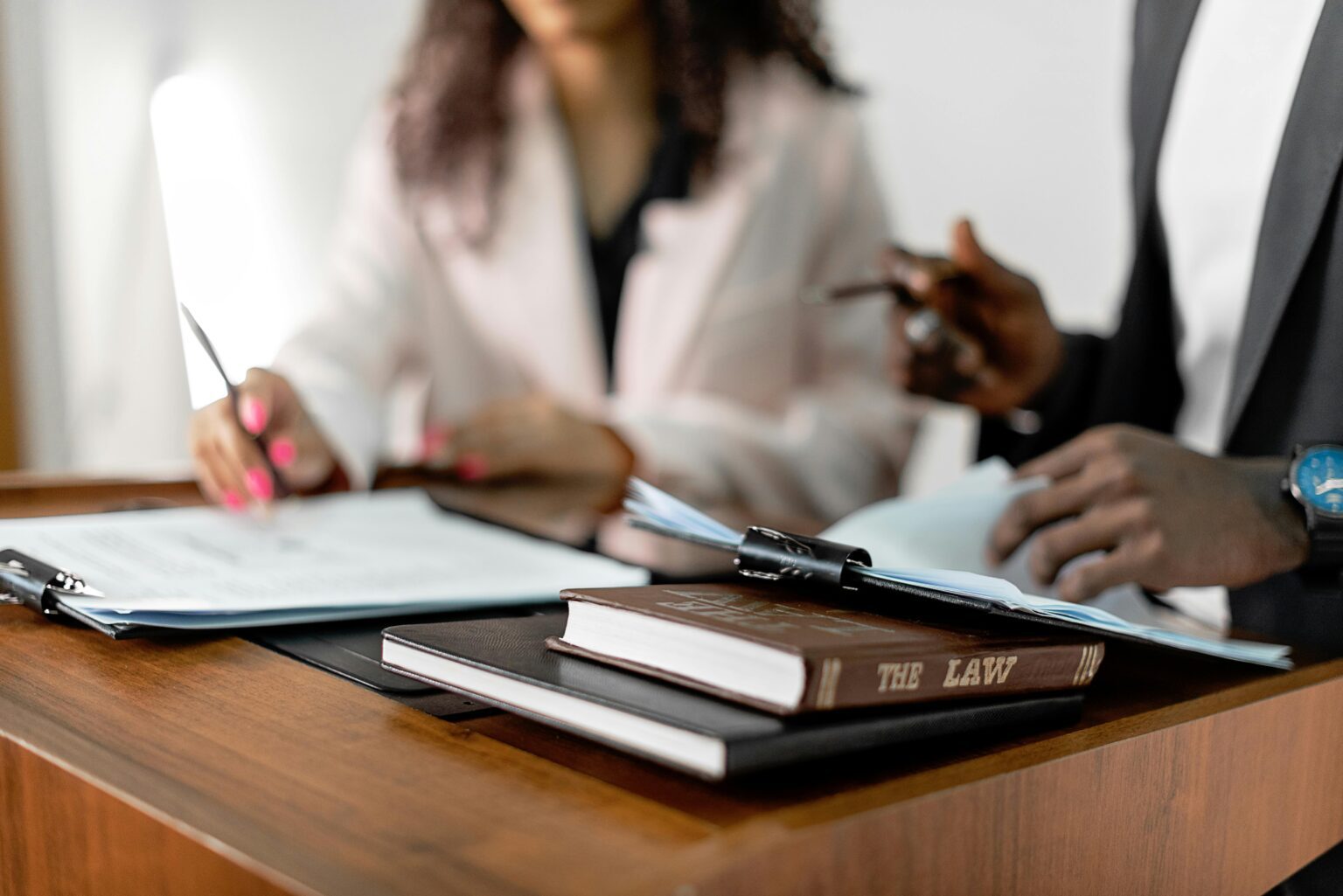 Two professionals reviewing documents at a desk next to a book titled The Law