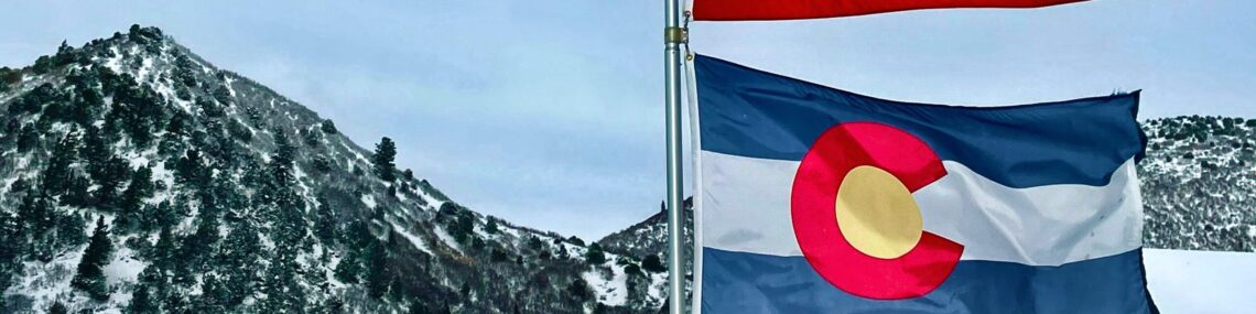 Colorado flag beneath American flag with mountains in background