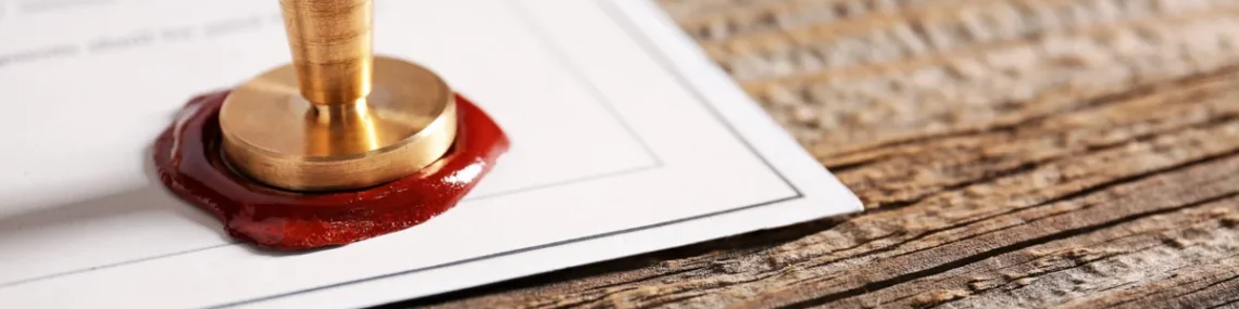 Brass wax seal pressed into red wax on a legal document resting on a rustic wooden desk