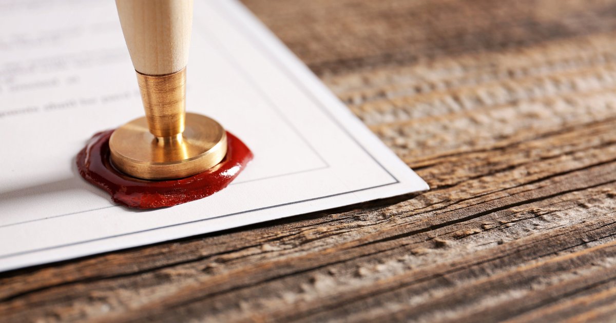 Brass wax seal pressed into red wax on a legal document resting on a rustic wooden desk