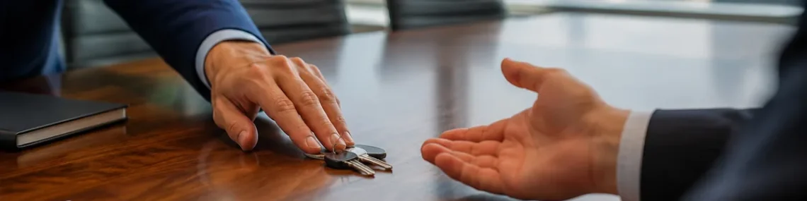 Business owner sliding a set of keys across a conference table to another person's open hand