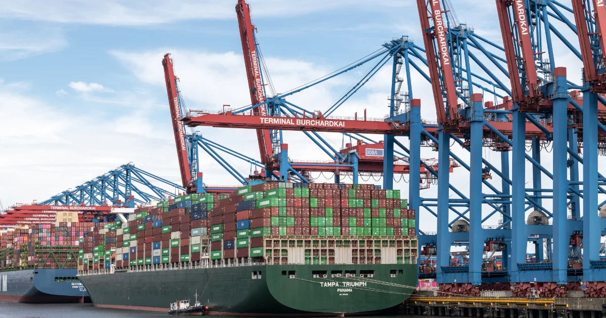 Container ship loaded with shipping containers under cranes at a port terminal