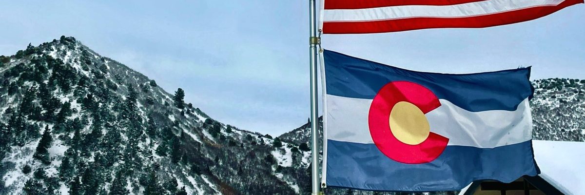 Colorado flag beneath American flag with mountains in background