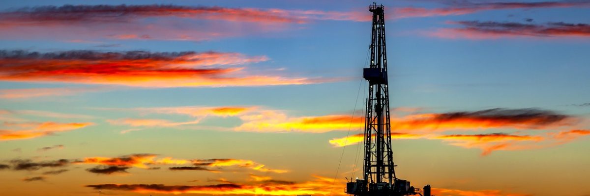 oil derrick in foreground with sun setting behind the rig